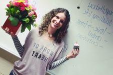 A woman standing in front of a whiteboard with flowers and a cupcake